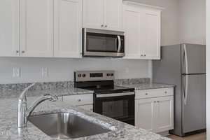 A modern kitchen features white cabinets, a granite countertop, a stainless steel oven with a black cooktop, a built-in microwave, a refrigerator, and a sink with a silver faucet.