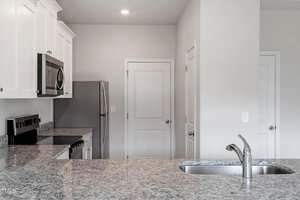 Modern kitchen with white cabinets, stainless steel appliances, granite countertops, an electric stove, built-in microwave, and a sink with a chrome faucet on an island. Three closed doors are visible in the background.