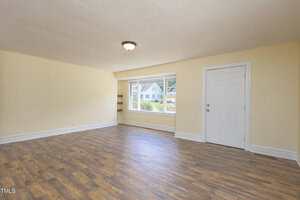 Unfurnished room with light yellow walls, wood-style flooring, a ceiling light fixture, a white door, and a large window with a view of houses and greenery outside.