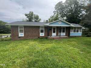Charming single-story brick house at 503 Adams Street in Henderson, featuring a black roof, white trim, and blue accents on the porch and sunroom, set on a grassy lawn with trees in the background.