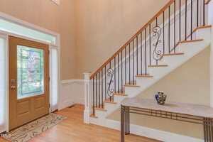 A foyer with a wooden front door featuring decorative glass, a staircase with wooden steps and black metal railings, and a console table with a patterned vase under the stairs.