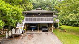 Located at 4144 Fairport Road in Kittrell, this raised house features a spacious screened-in porch, stairs to the entrance on the left, and an open parking area beneath for your car and boat, all surrounded by green trees and a grassy yard.