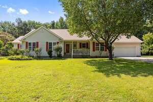 Charming single-story house at 3000 Hidden Spring Lane, Oxford, with white siding, red shutters, and a covered front porch. Features an attached two-car garage and sits on a well-kept lawn with a large tree and bushes in front.