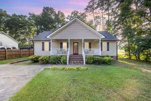 A single-story house at 609 N Country Club Drive in Oxford with gray siding and white trim, a covered front porch with railings, and steps leading up to the entrance, surrounded by shrubs and trees on a grassy lawn.