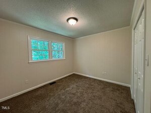 Empty room with beige walls, a textured ceiling, brown carpet, and a ceiling light fixture. Three windows on one wall provide natural light, and there are two closed doors on the right side.