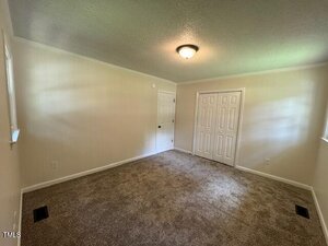 Empty room with beige carpet, cream-colored walls, a white ceiling, a ceiling light fixture, a closet with double doors, and two windows letting in natural light.