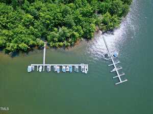 Aerial view of two boat docks extending from a forested shoreline into a greenish body of water, with multiple boats moored at the docks. Dense trees line the edge of the water.