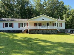 Charming single-story white house at 295 Georges Lane in Kittrell, featuring red shutters, a covered front porch, stone foundation, and steps leading to the entrance. Nestled on a green lawn with trees in the background.