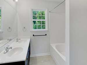 Bathroom with a double-sink vanity, a large mirror, a towel ring and bar, a window with green trees visible outside, and a white bathtub with a shower curtain rod.