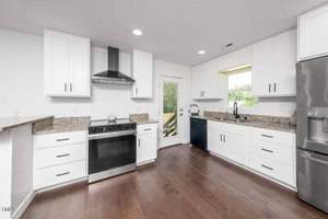 A modern kitchen with white cabinets, granite countertops, stainless steel appliances, a stove with a vent hood, a refrigerator, a dishwasher, and a window above the sink letting in natural light.