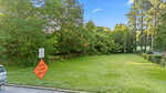 A grassy area bordered by trees and a fence near 1016 N Pinkston Street in Henderson, with a car partially visible on the left. Road signs read "End School Zone" and "Road Closed 500 Ft." The sky is clear and blue.