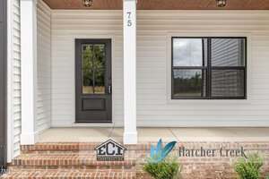 A front porch with brick steps, a black door with glass panes, white siding, a large window, house number 75, and logos for ECI Construction and Hatcher Creek displayed at the bottom right.