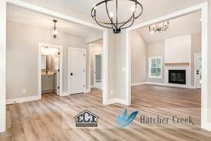 A modern home interior with light wood flooring, neutral walls, black metal chandeliers, a fireplace, large windows, and multiple doorways; ECI Construction and Hatcher Creek logos are visible in the foreground.