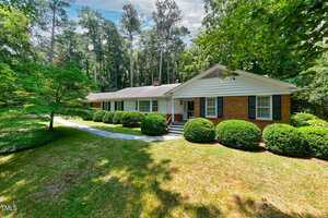 A single-story brick and white siding house at 225 Bellwood Drive in Henderson, with black shutters, is surrounded by neatly trimmed bushes and trees on a large grassy yard, featuring a stone walkway leading to the front steps.