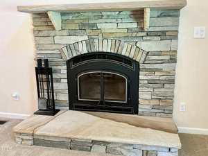 A stone fireplace with a black metal-framed glass door, a stone mantel, and a stone hearth. A black fireplace toolset stands on the left side, and electrical outlets are visible on the wall.
