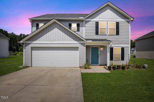 A two-story house with gray siding, black shutters, a blue front door, and a double garage sits at 443 Waterfall Road in Henderson. The home features a concrete driveway, small lawn, potted plants by the entrance, and a purple-pink dusk sky.