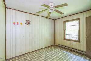 A small, empty room with wood panel walls, a patterned linoleum floor, a ceiling fan, a window, a door, three emoji stickers, and a crooked framed picture on the wall.