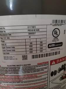 Close-up of a water heater label showing model number, manufacture date, capacity, voltage, wattage, and certification details, with safety warnings partially visible at the bottom of the label.