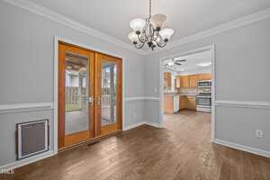 A dining area with wood flooring, a chandelier, French doors leading to a covered patio, and an open doorway to a kitchen with wooden cabinets and stainless steel appliances.