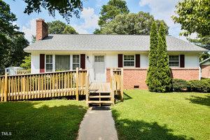 Located at 205 Forest Road, Oxford, this single-story house features a brick and white exterior, gray shingle roof, wooden accessibility ramp, and a well-kept lawn with shrubs and trees in the yard.