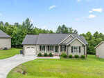 A single-story house at 421 Angus Place in Stem features gray siding, a dark roof, an attached single-car garage, front porch with white columns, and a well-kept lawn on a sloped driveway with trees and other homes in the background.