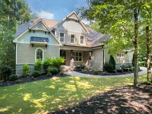 A two-story suburban house at 3575 Bragg Valley Lane in Wake Forest features beige siding, stone accents, and a dark roof, nestled behind a curved sidewalk amid green shrubs, manicured lawn, and trees on a sunny day.