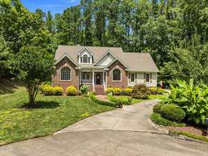 A single-family house with brick and light siding, arched windows, and a gabled roof, set among trees with a curved driveway and landscaped front yard.