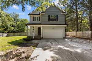 A two-story suburban house at 611 30th Street in Butner with gray siding, black shutters, a covered front porch, and double garage. The concrete driveway leads to a fenced yard with trees and grass surrounding the home.