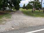 A gravel driveway off 00 Bullocksville Park Road in Manson leads into a grassy yard with trees. A white mobile home and a brick house are visible, along with parked cars and a red shed in the background.