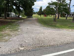 A gravel driveway off 00 Bullocksville Park Road in Manson leads into a grassy yard with trees. A white mobile home and a brick house are visible, along with parked cars and a red shed in the background.