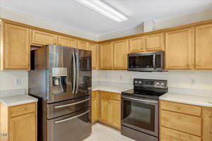 A kitchen with light wood cabinets, a stainless steel French door refrigerator, a black electric stove with a matching microwave above it, and light-colored countertops.
