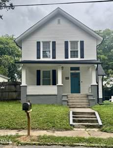 A two-story white house with black shutters and a turquoise front door at 128 Carolina Avenue in Henderson, featuring a covered porch, gray steps, and a small front lawn with a mailbox by the sidewalk. Trees and neighboring homes are in the background.