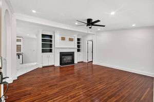 A living room with hardwood floors, white walls, a black ceiling fan, built-in shelves and cabinets surrounding a fireplace, and an open doorway leading to a tiled area in the background.