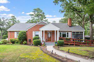 A single-story red brick house at 602 18th Street in Butner features a gabled roof, wooden front door, bushes along the front, a wheelchair-accessible ramp on the right, and a curved concrete walkway leading to the porch.