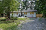 A single-story white house at 605 26th Street, Butner, with yellow-trimmed windows, a black front door, metal railings, and a gravel driveway, surrounded by trees and greenery.