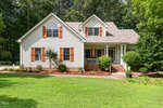 A two-story suburban house at 235 Highview Drive in Youngsville with white siding, brown window shutters, a cozy front porch, and a well-kept lawn bordered by mulch and shrubs, surrounded by trees in the background.