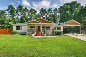 Charming single-story home at 3649 Windsor Drive, Franklinton, featuring white siding, a front porch with red steps, and a carport on the right. Enjoy the green lawn, mature trees in the background, and a partly cloudy sky overhead.