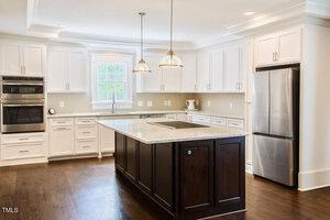 Spacious kitchen with white cabinets, stainless steel appliances, a double oven, and a large island with dark wood base and marble countertop. Two pendant lights hang above the island.