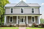 A two-story house at 611 College Street in Oxford features gray siding, a metal roof, and white trim with a covered front porch supported by white columns, brick steps, and a landscaped front yard with bushes and a brick walkway.