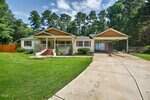 Charming single-story house at 3649 Windsor Drive, Franklinton, with white siding and yellow trim, a front porch with brick steps, attached carport, concrete driveway, green lawn, and trees under a partly cloudy sky.