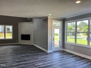 Unfurnished living room with gray wood-look floors, light gray walls, large windows, a white door with glass panels, and a built-in fireplace set into a shiplap accent wall. Natural light fills the space.