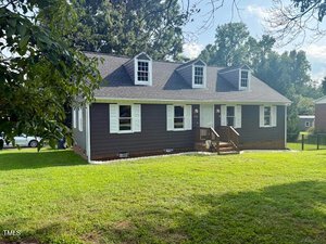 A brown, single-story house with three dormer windows and a small front porch sits on a well-maintained lawn at 105 Meadow Brook Lane, Oxford. The home features white trim, with trees and other houses visible in the background.