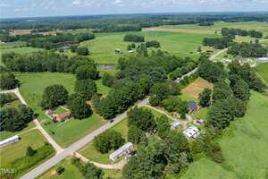 A rural landscape near 2535 Warrenton Road, Henderson, with scattered houses, roads, and dense green trees surrounded by fields and farmland under a partly cloudy sky, photographed from above.