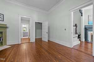 Empty room with light-colored walls, wooden floor, white trim, and an open closet. Two doorways lead to other rooms; one shows a staircase and another a bathroom with a window and vanity. A small built-in shelf is on the left.