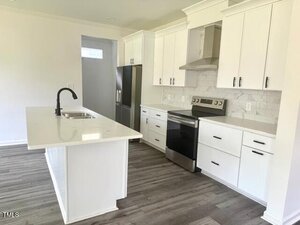 Modern kitchen with white cabinets, a stainless steel refrigerator and stove, a marble backsplash, and a center island with a sink and black faucet; the floor is gray wood-style laminate.