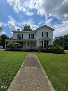 A white two-story house with black shutters and a covered front porch sits at 412 Kingsbury Street, Oxford, framed by green grass, bushes, and trees under a partly cloudy sky.
