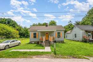 A small, single-story house at 810 Vaughan Street in Henderson features yellow shutters and an orange front door behind a stone walkway. A white car is parked on the grass to the left, with a neighboring house visible on the right.