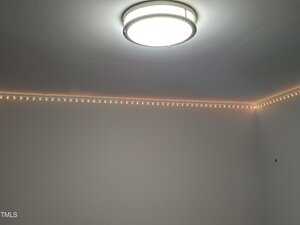 A ceiling light fixture is turned on, illuminating a room with white walls. There is a strip of small LED lights installed along the top corner where the walls meet the ceiling.
