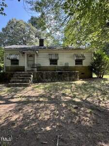 A small, single-story house with white siding and a stone foundation sits at 716 Williamsboro Street in Oxford. It features three front windows with metal awnings, a central door, concrete steps, and a yard with trees and patchy grass.