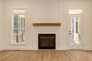 A living room features a gas fireplace with a wood mantel, white shiplap accent, two tall windows, and a glass door leading to a screened porch. The floors are light wood, and the walls are painted white.